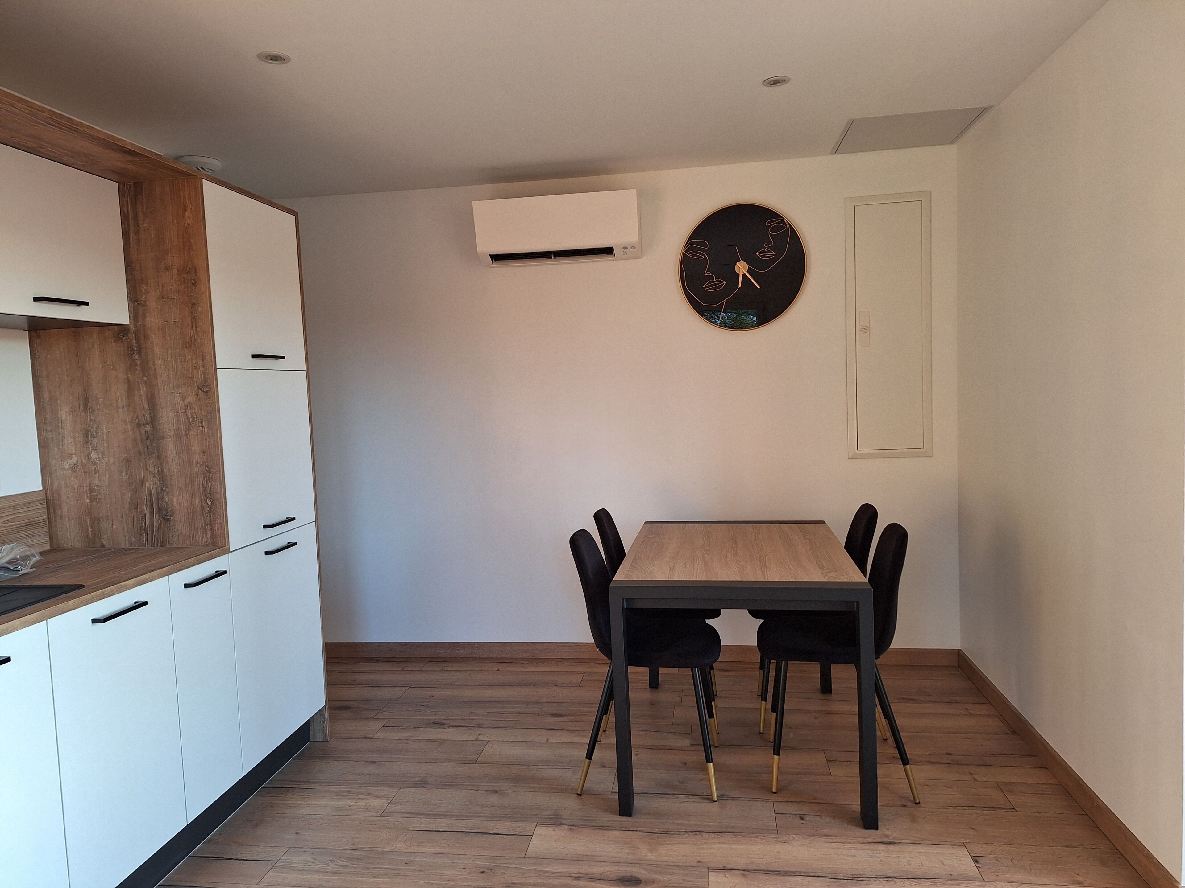 A modern kitchen with white cabinets and a wooden countertop, a dining area with a wooden table and black chairs, and a wall-mounted clock.