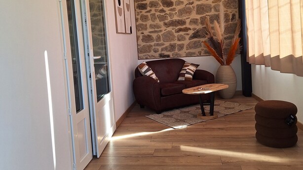 Una sala de estar con una pared de piedra, un sofá de cuero marrón, una mesa de centro de madera y un jarrón grande con plantas secas.
