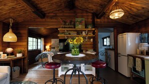 A rustic wooden interior with a round dining table, bar stools, a television, and a kitchen area with a refrigerator and microwave.