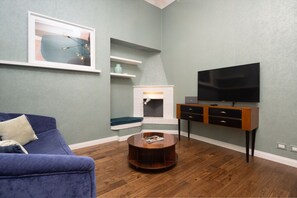 A living room with a blue sofa, a round wooden coffee table, a fireplace, a TV on a wooden stand, and a framed picture on the wall. - Fossi Street Central Apartment (Florence)