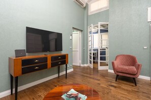 A living room with a flat-screen TV on a wooden console, a red armchair, and a wooden coffee table with magazines.