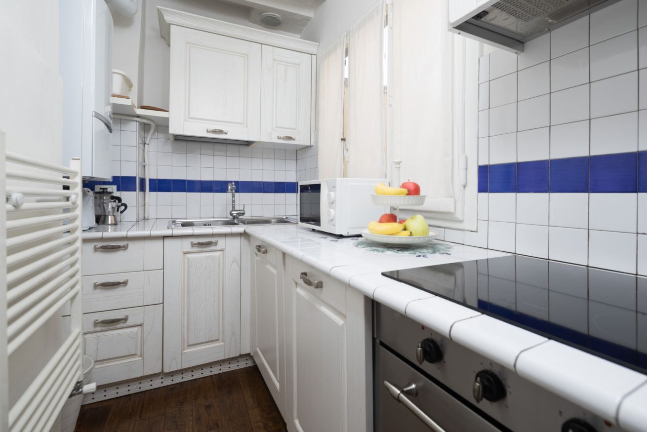 A kitchen with white cabinets, a microwave, a stove, and a fruit basket.