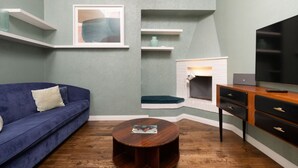 A living room with a blue sofa, a round coffee table, a fireplace, a TV, and built-in shelving. - Fossi Street Central Apartment (Florence)