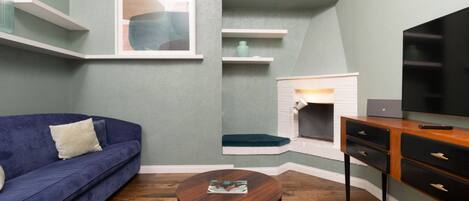 Una sala de estar con un sofá azul, una mesa de centro redonda, chimenea, televisor y estanterías empotradas.