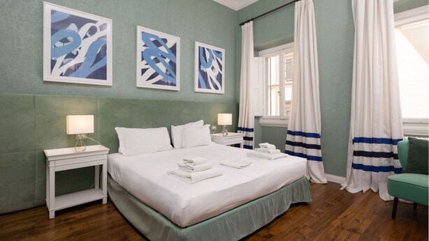 A neatly made bed with white linens and folded towels, a bedside table with a lamp, and a window with curtains. - Fossi Street Central Apartment (Florence)