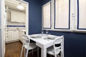 A compact kitchen with white cabinets, a white countertop, and a window with blinds.