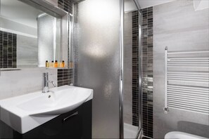 A modern bathroom with a white sink, a mirror, and a glass shower enclosure.