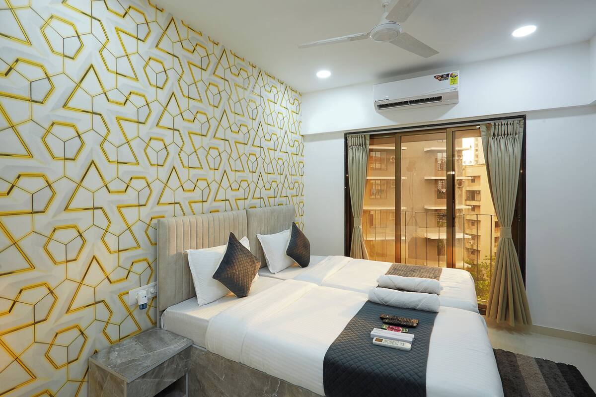 Une chambre d’hôtel avec un mur orné d’un motif géométrique, un ventilateur de plafond, un appareil de climatisation et une vue sur l’extérieur par une porte vitrée.