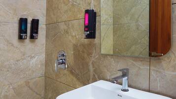 A modern bathroom with a white sink, a handheld showerhead, and two shampoo dispensers mounted on the wall.