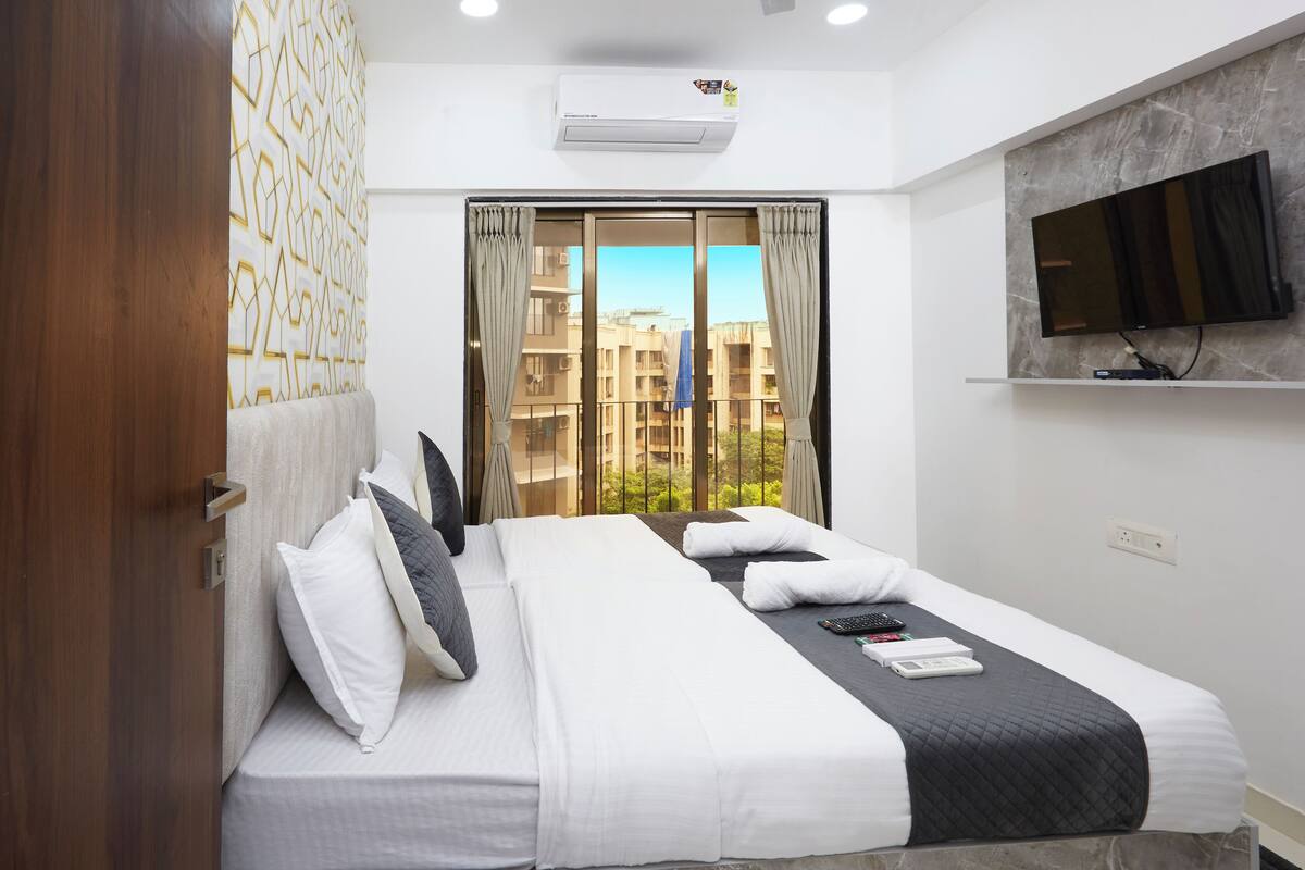 Une chambre d’hôtel moderne avec un grand lit, un téléviseur à écran plat fixé au mur et une vue sur la ville par la fenêtre.