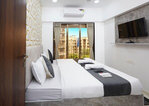 A modern hotel room with a large bed, a flat-screen TV mounted on the wall, and a view of the city through the window. - Astha Powai Service Apartments (Mumbai)
