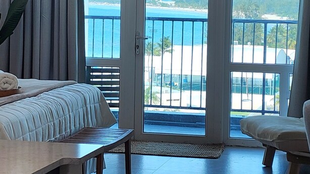 Een slaapkamer met een bed, een stoel, een tafel en uitzicht op de oceaan door een schuifdeur.