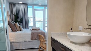 Een moderne slaapkamer met een groot bed, een houten stoel, een badkamer met een grote wastafel en donkerhouten kastjes.