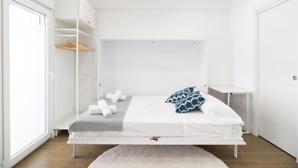A minimalist bedroom with a bed, a wardrobe, and a small table. - Waou Terrace House I (Madrid)