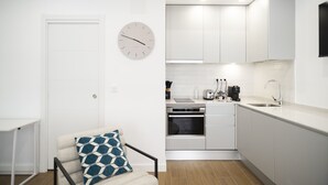 A compact kitchen with white cabinets, a built-in oven, a coffee maker, and a clock on the wall. - Waou Terrace House I (Madrid)