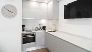 A modern kitchen with white cabinetry, a built-in oven, a sink, and a flat-screen TV mounted above the counter. - Waou Terrace House I (Madrid)
