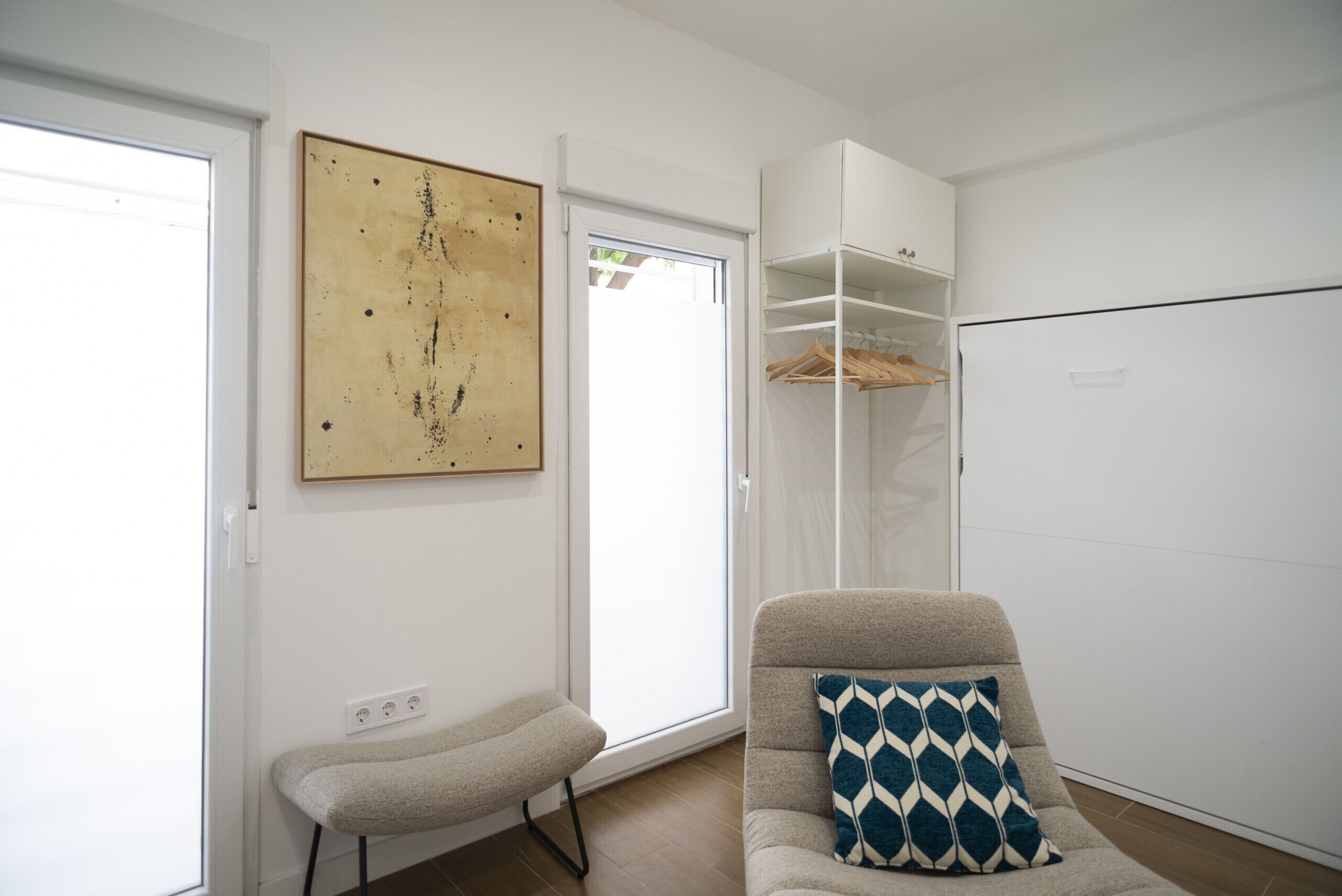 A modern living room with a sofa, a bench, a large abstract painting, a wardrobe, and a window.