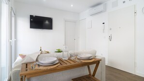 A modern, well-lit room with a dining table set for two, a flat-screen TV mounted on the wall, and a white door. - Waou Terrace House III (Madrid)