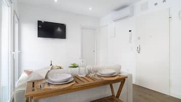 Een moderne, goed verlichte kamer met een eettafel voor twee personen, een wandtelevisie en een witte deur.