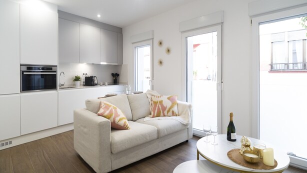 A modern kitchen with white cabinets, a built-in oven, and a dining area with a white table and a sofa. - Waou Terrace House III (Madrid)