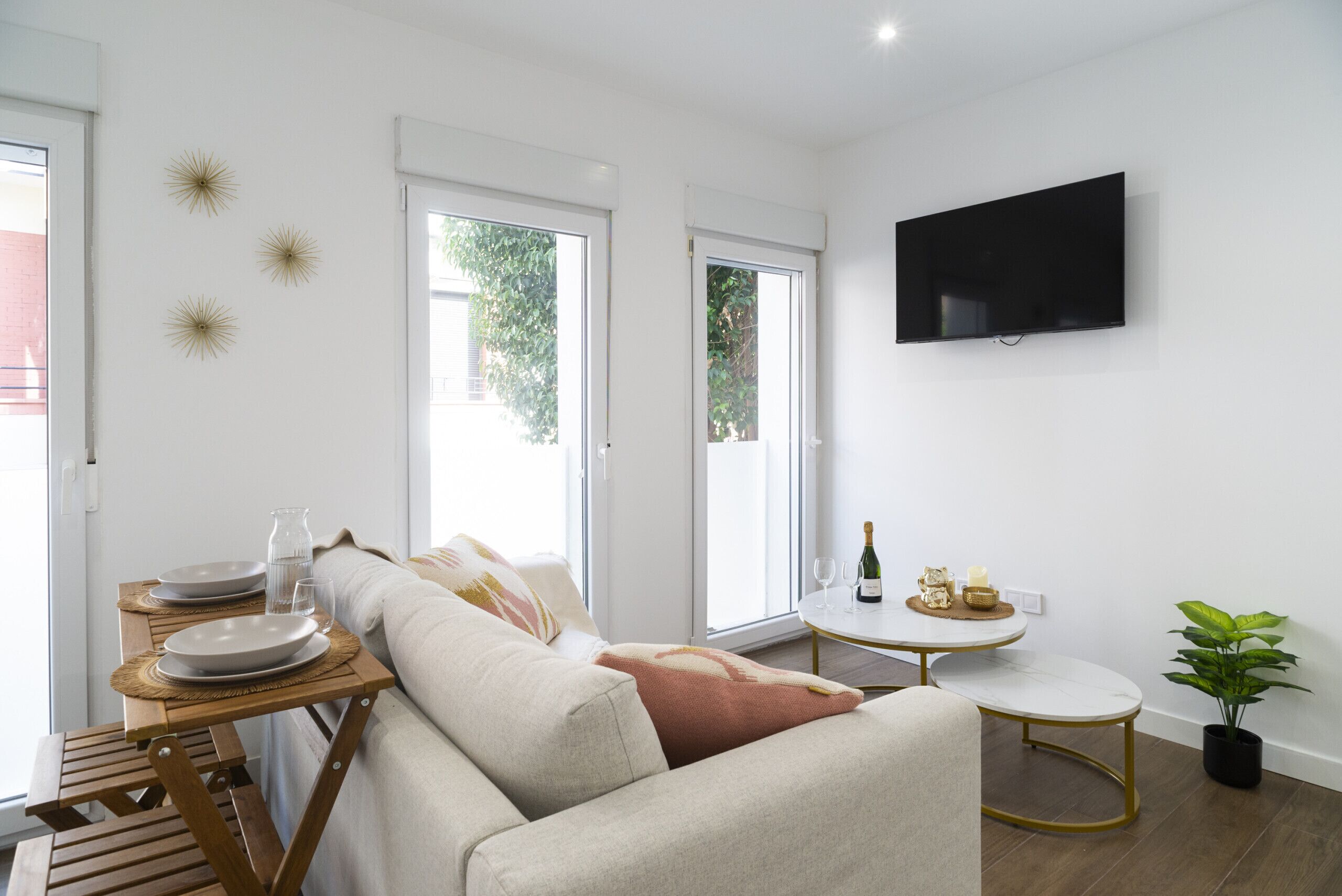 Een moderne woonkamer met een bank, een klein rond tafeltje met een televisie, en een groot raam met uitzicht op groen.