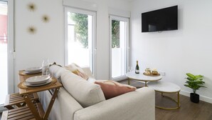 A modern living room with a sofa, a small round table with a TV, and a large window with a view of greenery. - Waou Terrace House III (Madrid)