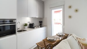 A modern kitchen with white cabinets, a built-in oven, a sink, and a dining area with a wooden table and chairs. - Waou Terrace House III (Madrid)