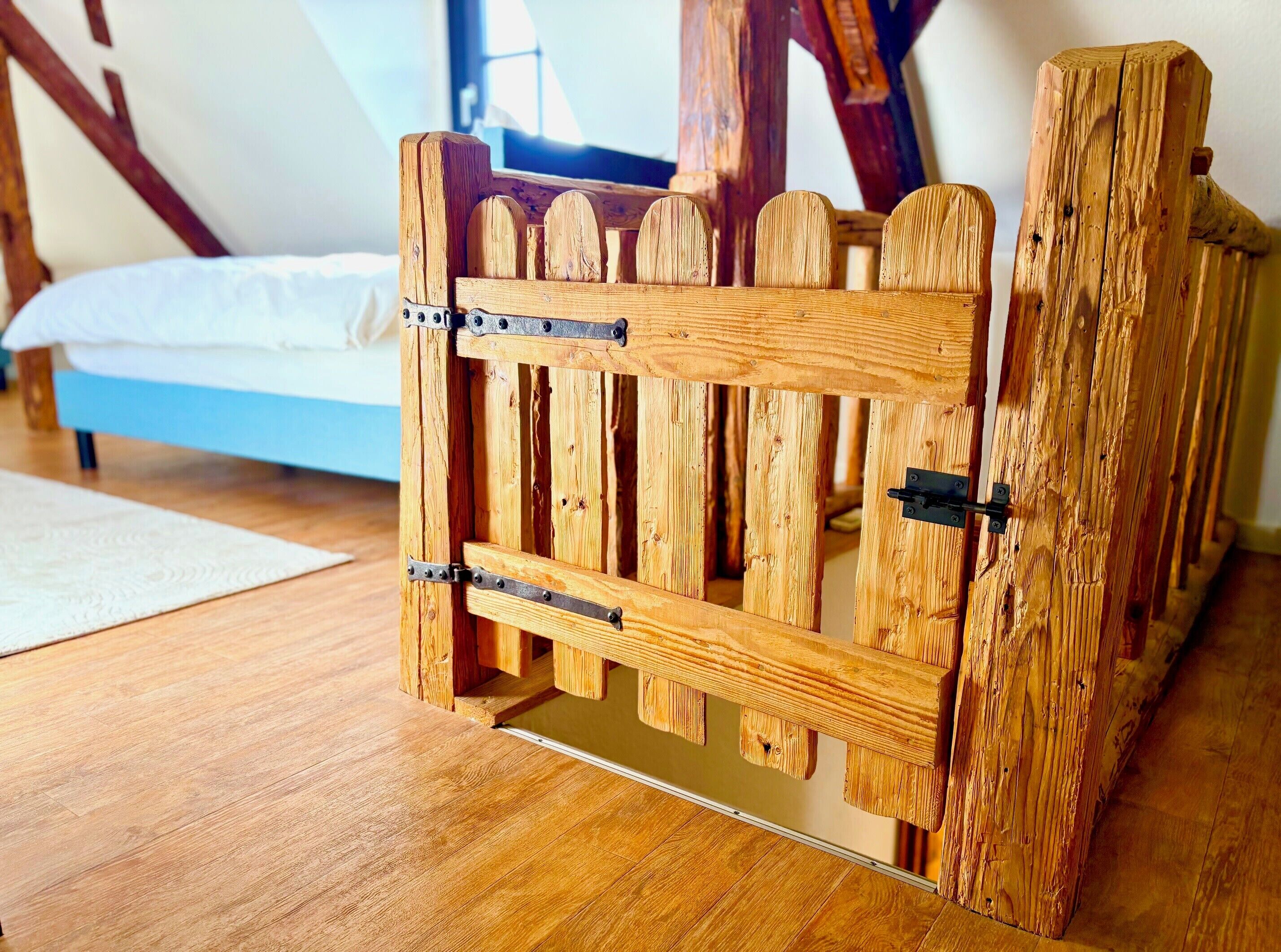 A wooden gate with metal hinges in a room with a bed and a window.