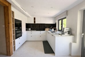 A modern kitchen with white cabinetry, a black backsplash, and a window providing natural light.