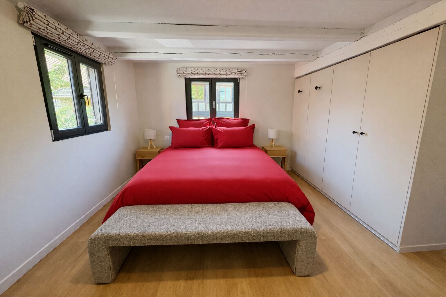 A bedroom with a bed, bedside tables, a bench, a wardrobe, and a window.