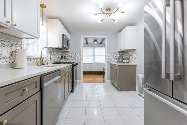 A modern kitchen with white cabinets, stainless steel appliances, and a tiled backsplash. - Comfy Nest ~ 3BR Sleeps 7 ~ 15 mins to Hartford (Manchester)