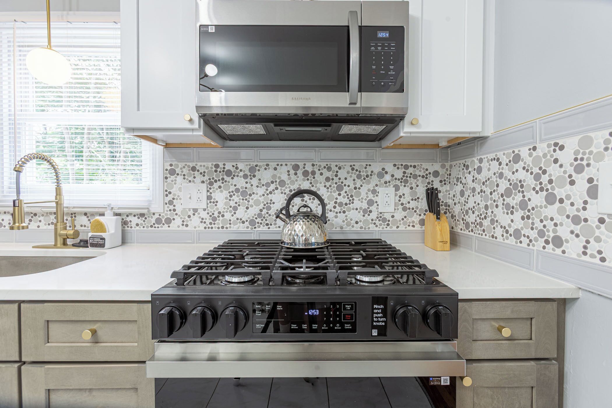 A kitchen with a stainless steel range hood, a microwave, a gas stove, and a kettle.