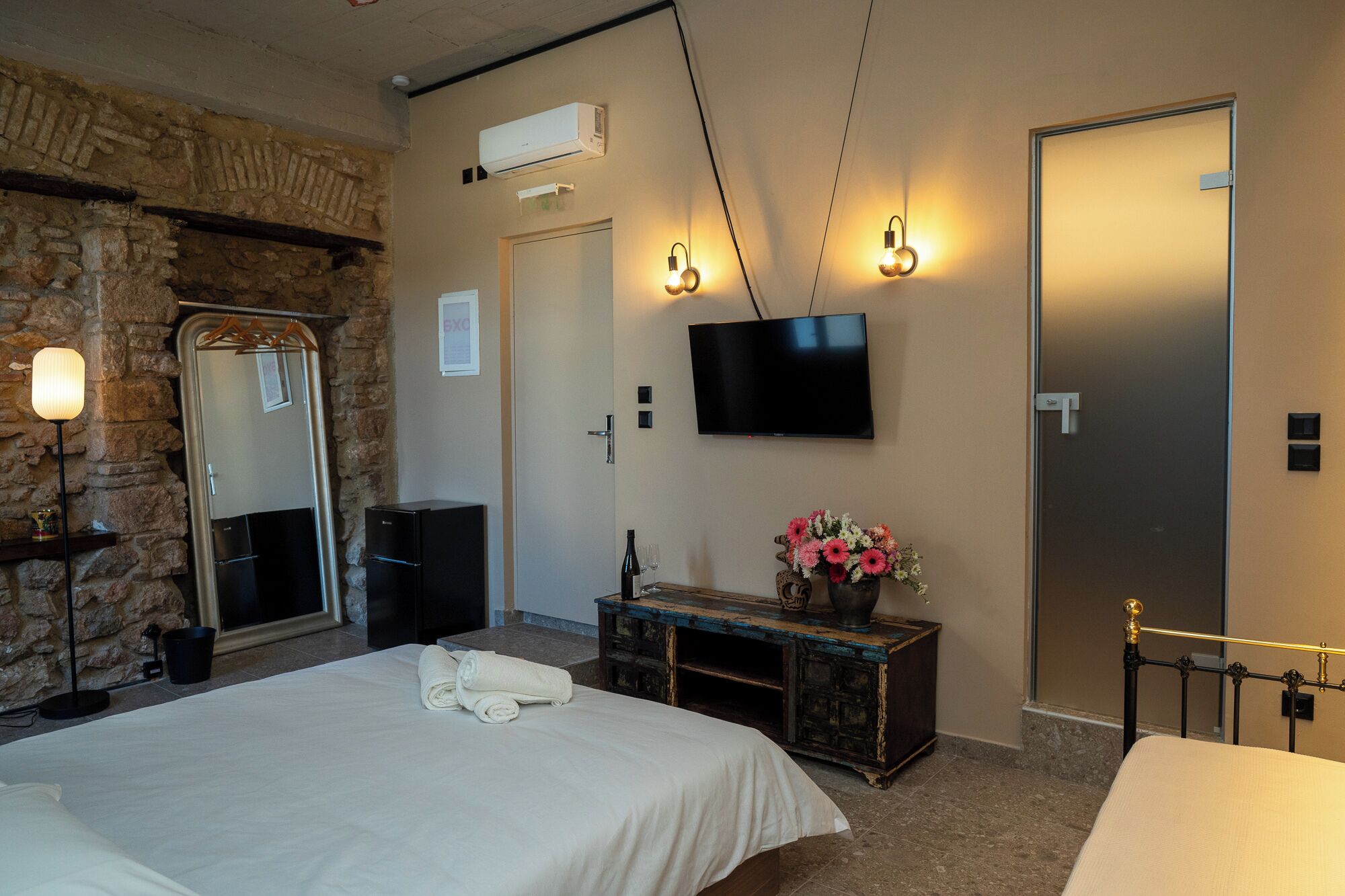 Een hotelkamer met een bed, een kaptafel, een spiegel, een televisie en een stenen muur.