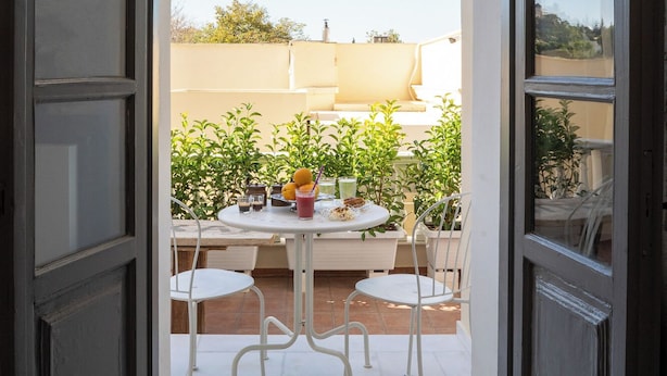 Eine offene Tür, die auf eine Außenpatio mit Tisch und Stühlen führt, umgeben von Grünpflanzen.