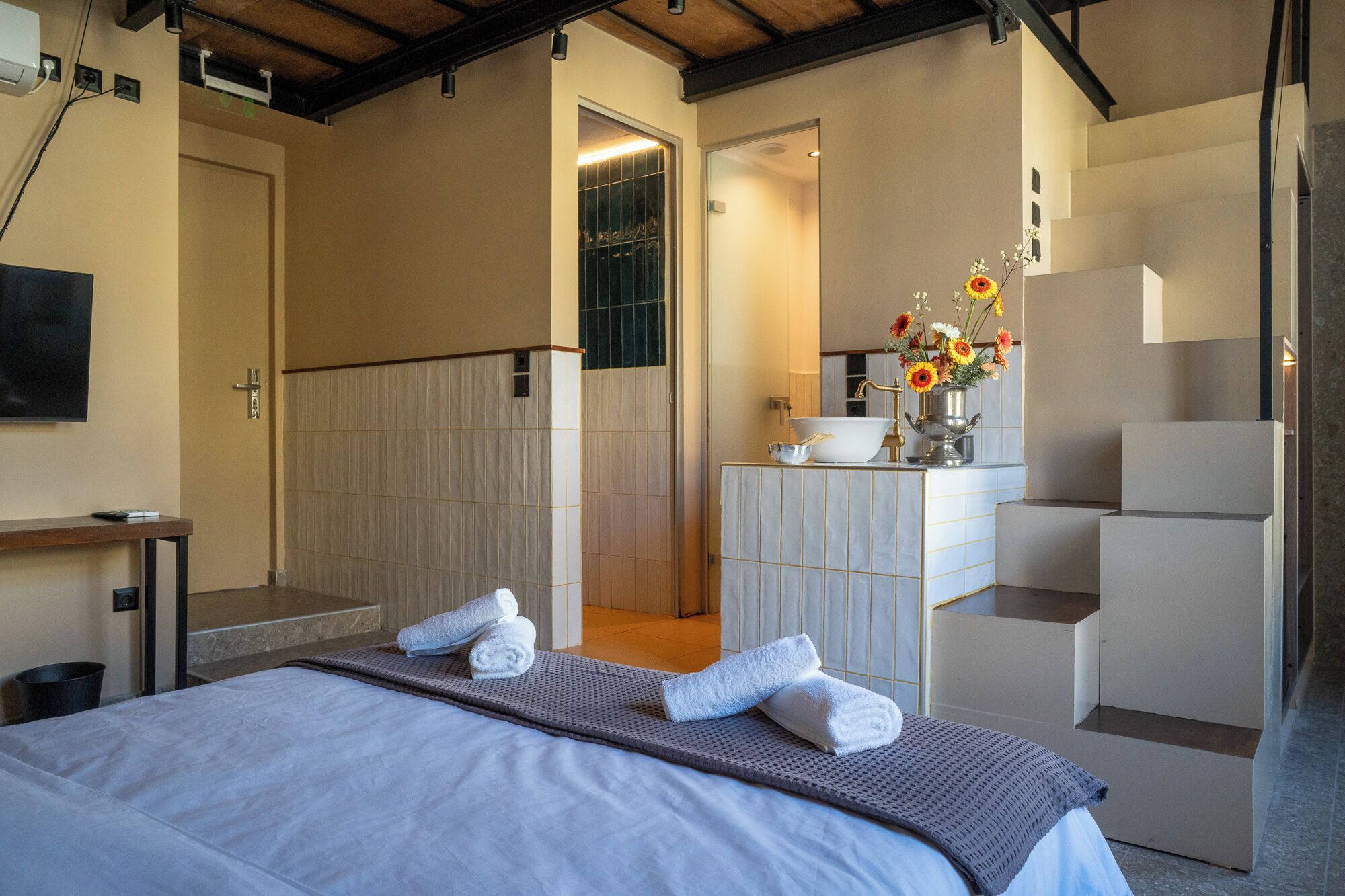 A hotel room with a bed, a bathroom with a sink and mirror, and a small table with a TV.