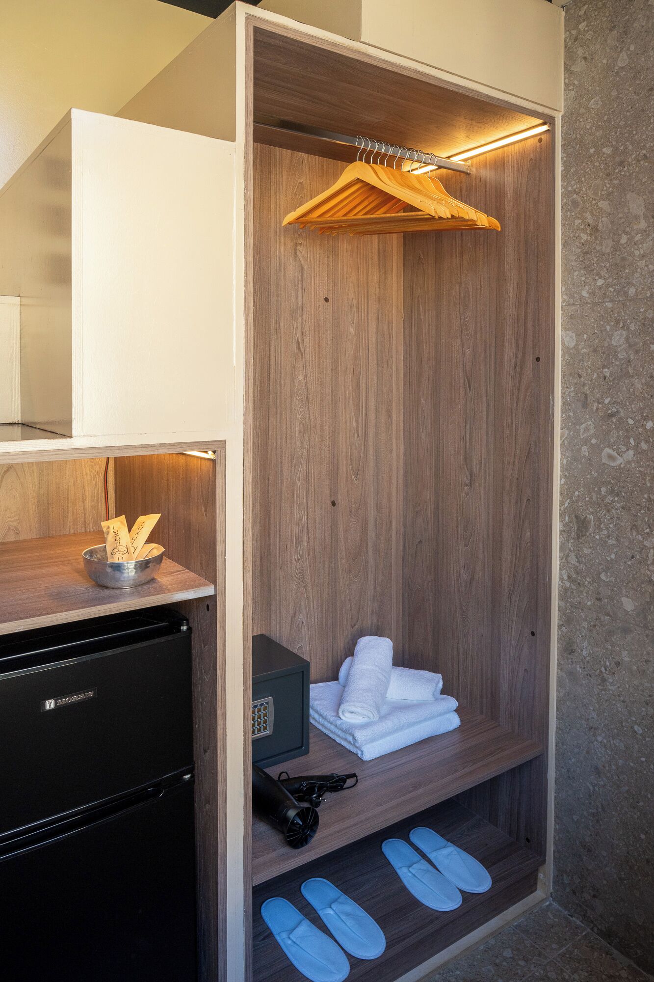 Un baño pequeño con un tocador de madera, un electrodoméstico negro, un perchero y un par de pantuflas.