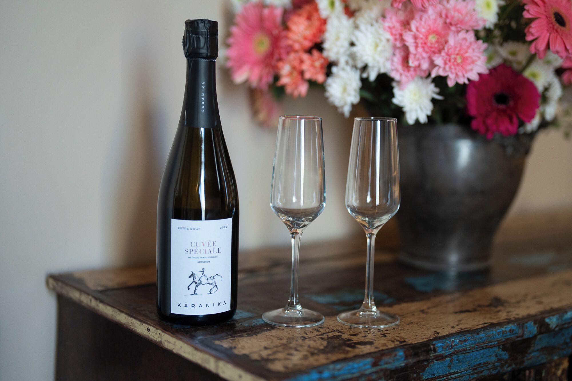 Une bouteille de vin, deux verres vides et un vase de fleurs sur une table en bois rustique.