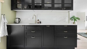 Una cocina con armarios oscuros, encimera blanca y hervidor de acero inoxidable.