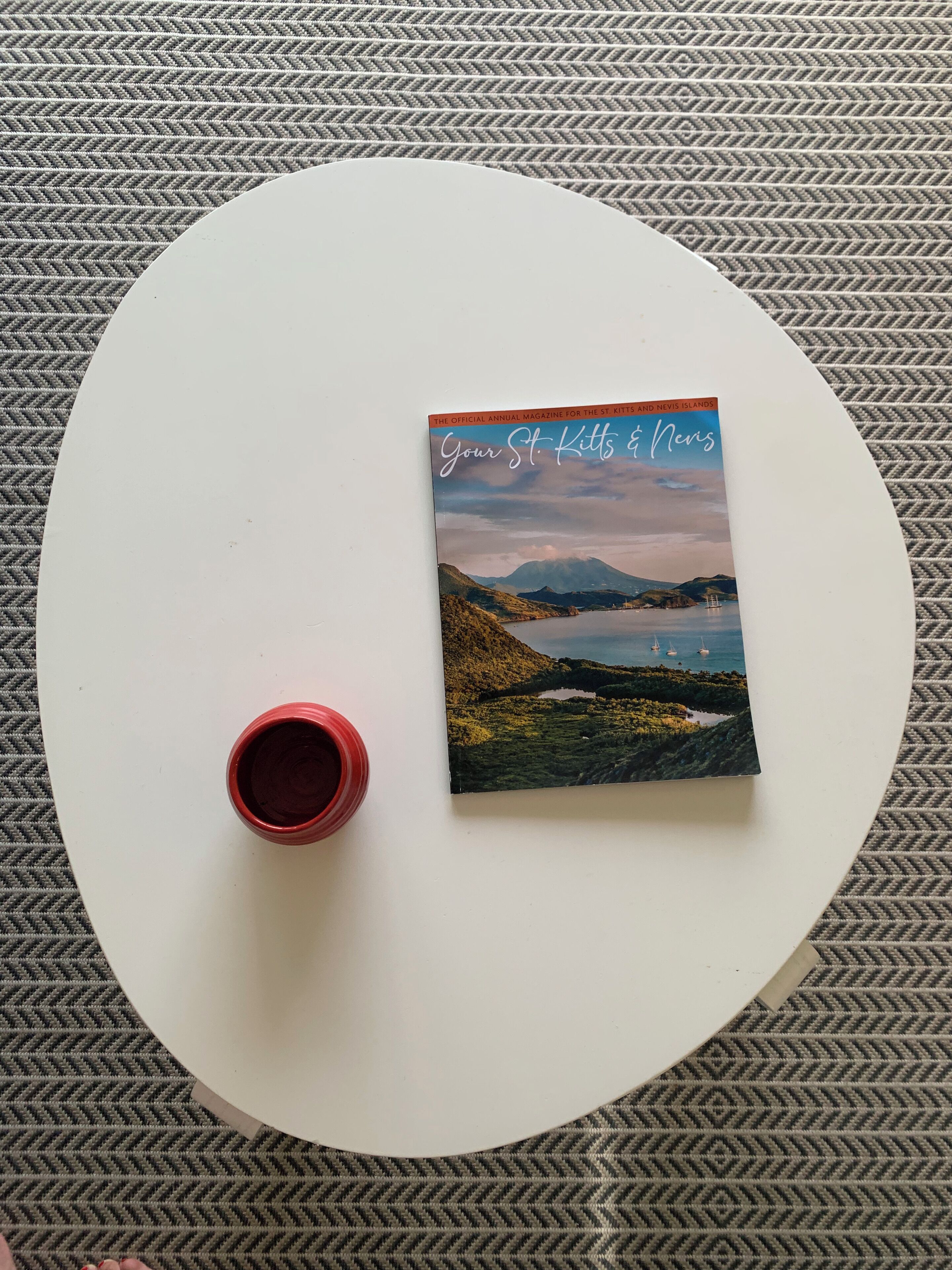 Ein weißer Tisch mit einem Buch mit dem Titel "Your St. Kitts & Nevis" und einer roten Tasse darauf.