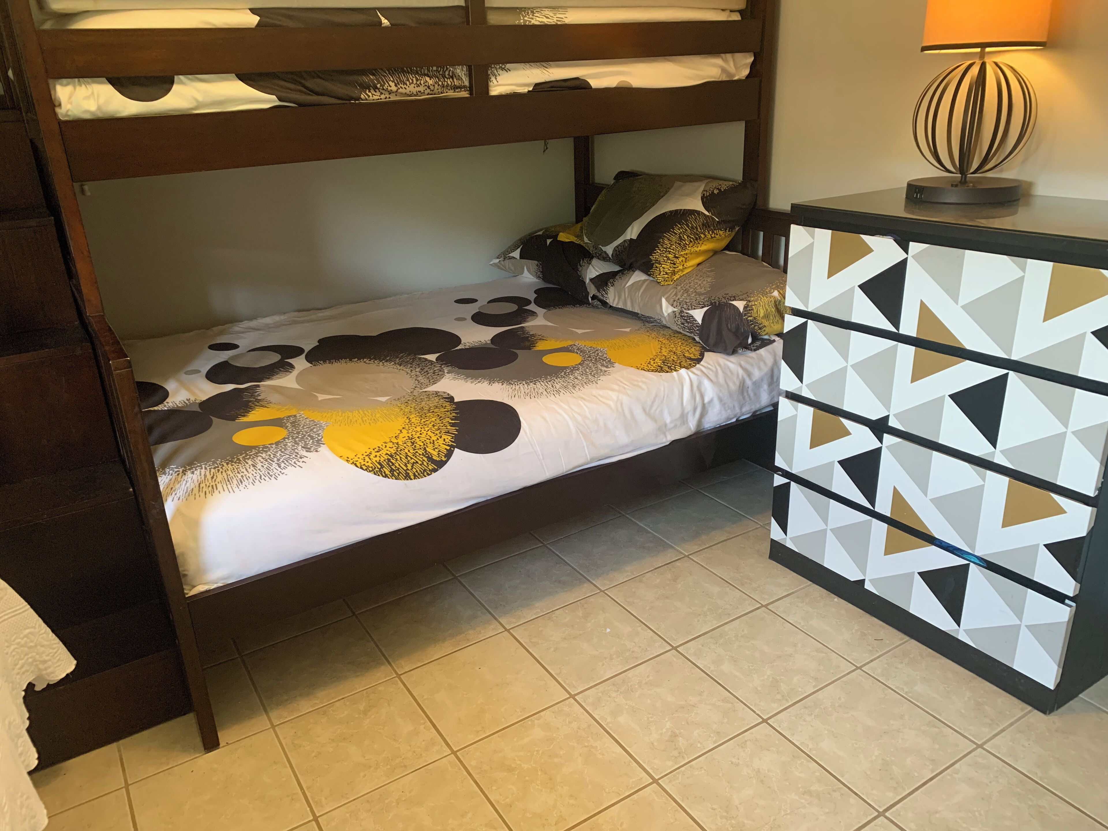 A bunk bed with a patterned bedspread, a bedside table with a geometric design, and a lamp.