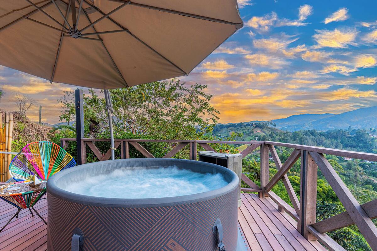 A hot tub on a wooden deck with a view of mountains and a colorful chair.