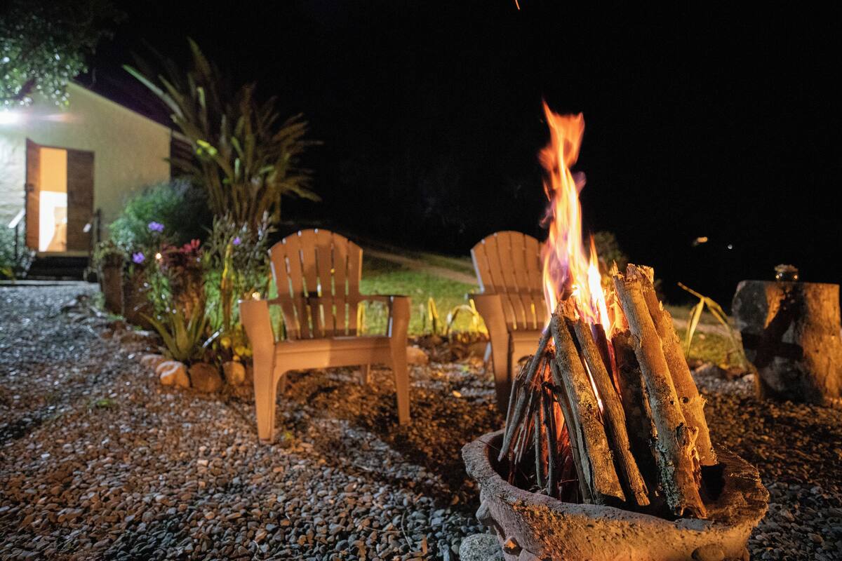A fire pit with logs, surrounded by chairs and a gravel path.