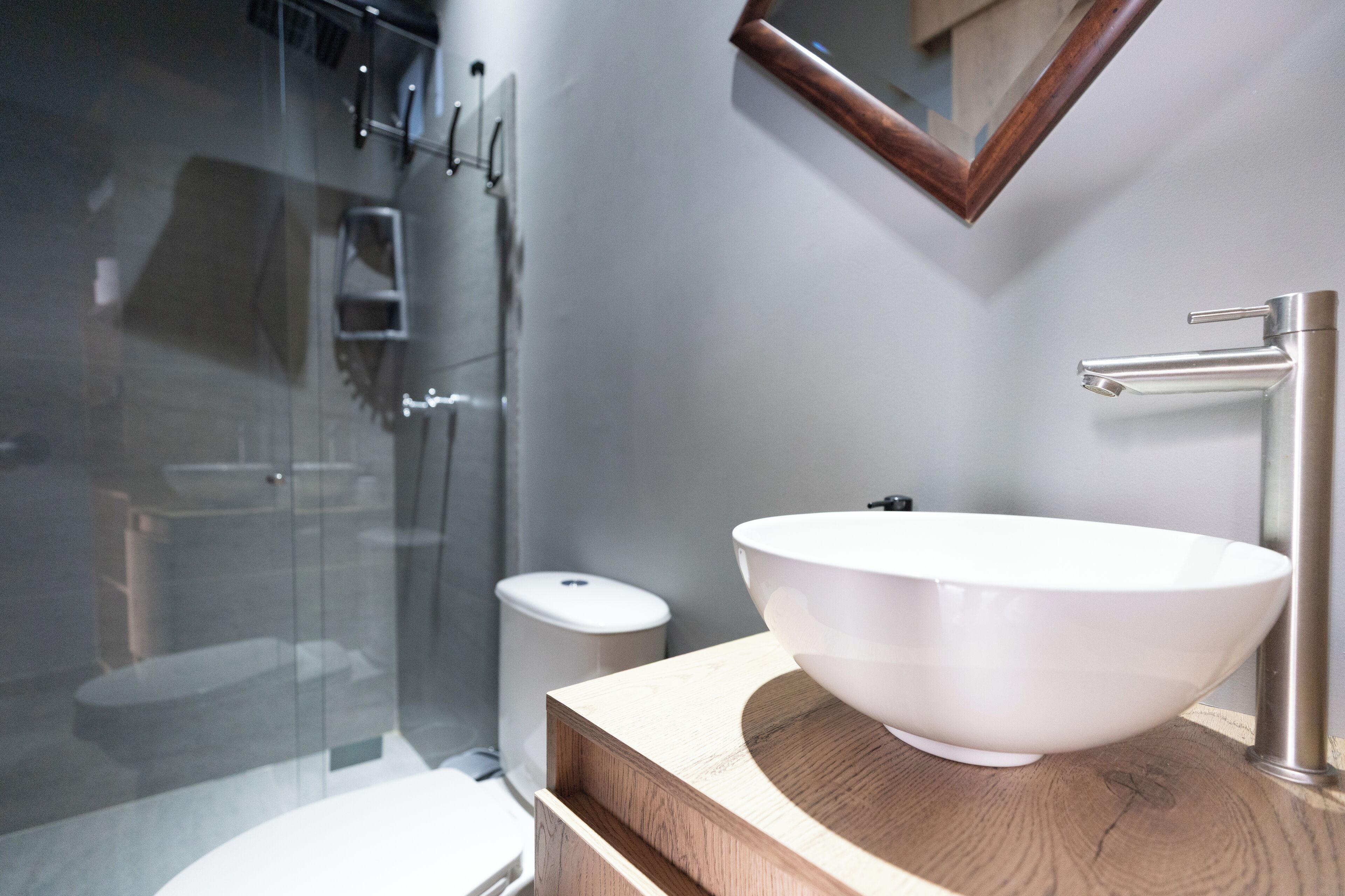 Ein modernes Badezimmer mit einem großen weißen Waschbecken, einer Holz-Waschkonsole, einer Glasdusche und einer kleinen weißen Toilette.