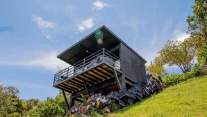A modern, elevated structure with a balcony, surrounded by lush greenery and a clear sky. - Roots Eco House (El Peñol)