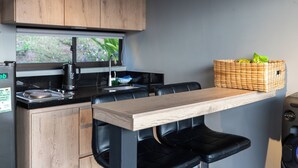A modern kitchen with wooden cabinets, a black countertop, a built-in stove, and a window with a view of greenery. - Roots Eco House (El Peñol)