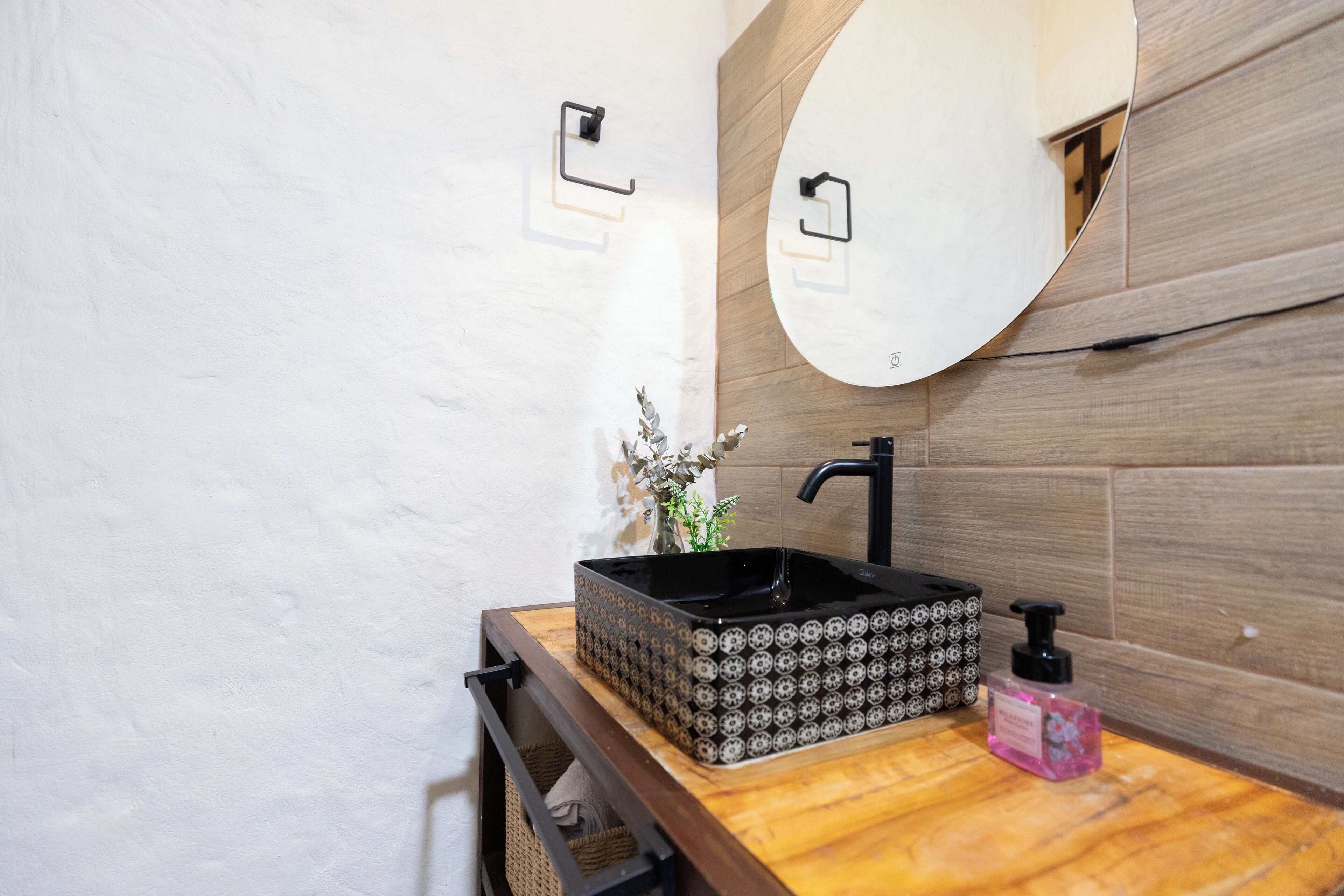 Een badkamer met een houten wastafelmeubel, een zwarte wastafel met een decoratieve kom, een spiegel en een kleine plant.