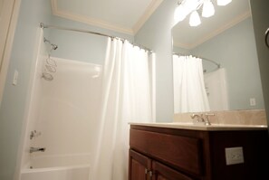 A bathroom with a shower, a vanity with a mirror, and a light fixture above the mirror.