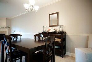 A dining room with a dark wooden table, six chairs, a chandelier, a mirror, and a sideboard with glassware.
