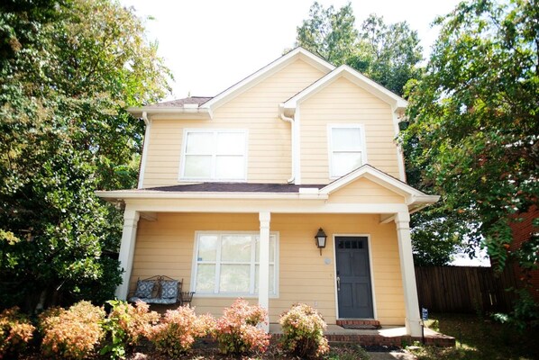 A two-story house with a front porch, a garage door, and a front yard with shrubs.