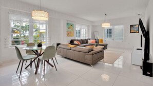 A spacious living room with a large sofa, a dining area with chairs and a table, and a flat-screen TV mounted on the wall.